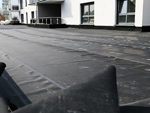 EPDM-Roofing-Elizabethtown-KY-Kentucky-1 | Commercial Roofing Pros Flat rooftop with black waterproof membrane, a modern white building with windows and balconies visible in the background.
