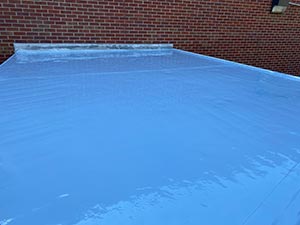 Rubber-Roof-Coating-Campbellsville-KY-Kentucky-1 | Commercial Roofing Pros Blue tarp covering a flat roof with a brick wall in the background, secured around the edges.