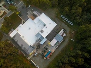 Aerial view of a white, multi-wing building campus surrounded by trees, with a parking lot nearby.