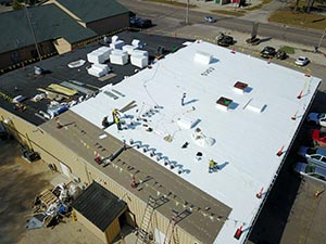 flat-roof-installation-Elizabethtown-KY-Kentucky-2 | Commercial Roofing Pros Aerial view of a flat-roofed commercial building with workers and equipment installing on the white roof surface down below the surrounding area visible.