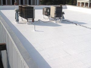 Three outdoor air conditioning condenser units mounted on a white flat roof with a railing along the edge.